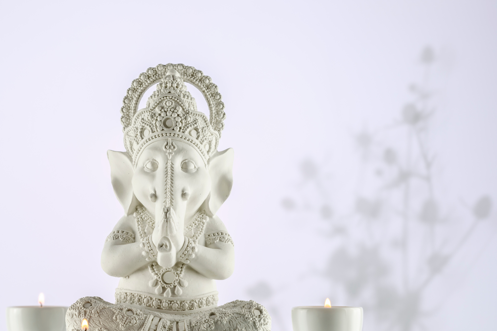 Sculpture of Lord Ganesha with candles on a gradient light background with shadows and copy space. Holiday of Ganesh Chaturthi. Ganesh festival. Hindu religion holidays. Front view