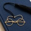 Gold plated brass Gandhi spectacles bookmark with black tassel placed on a navy blue jute fabric covered book, minimalist premium Indian gift for readers