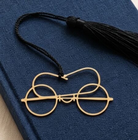 Gold plated brass Gandhi spectacles bookmark with black tassel placed on a navy blue jute fabric covered book, minimalist premium Indian gift for readers
