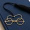 Gold plated brass Gandhi spectacles bookmark with black tassel placed on a navy blue jute fabric covered book, minimalist premium Indian gift for readers