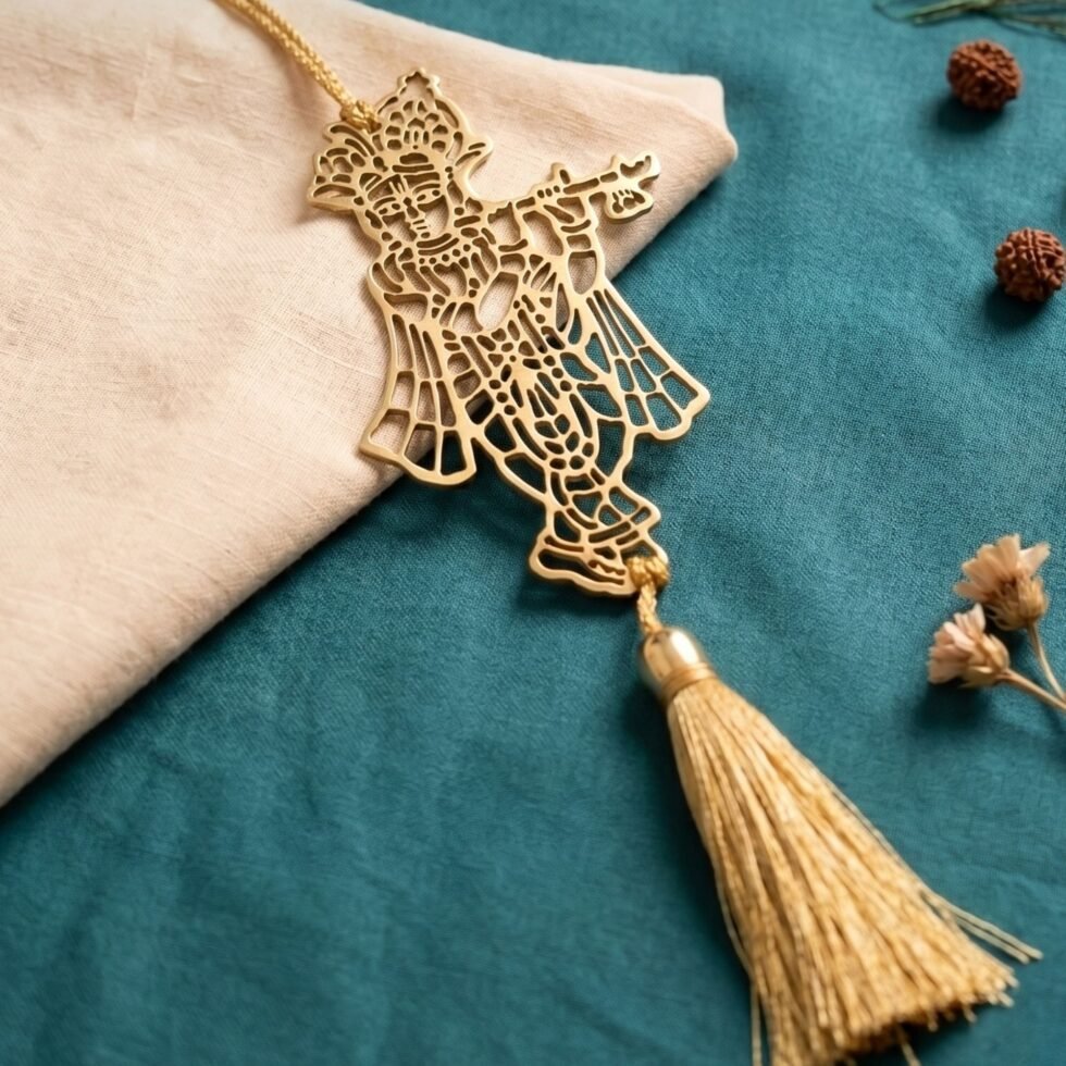 Brass Krishna flute hanging decor with tassel placed diagonally on teal fabric with peacock feather and rudraksha beads.