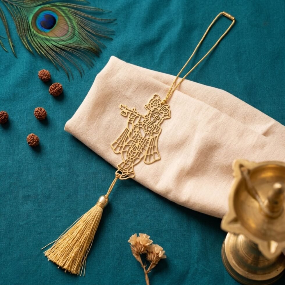 Gold polished brass Krishna hanging decor with tassel displayed on cream fabric pouch over teal background.