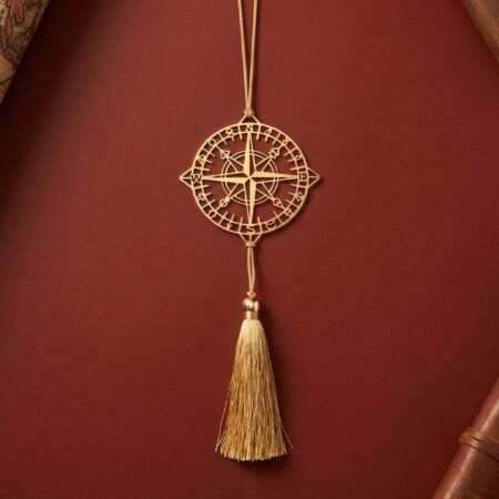 Gold polished brass compass hanging decor with tassel displayed on a barn red textured background in elegant minimalist styling