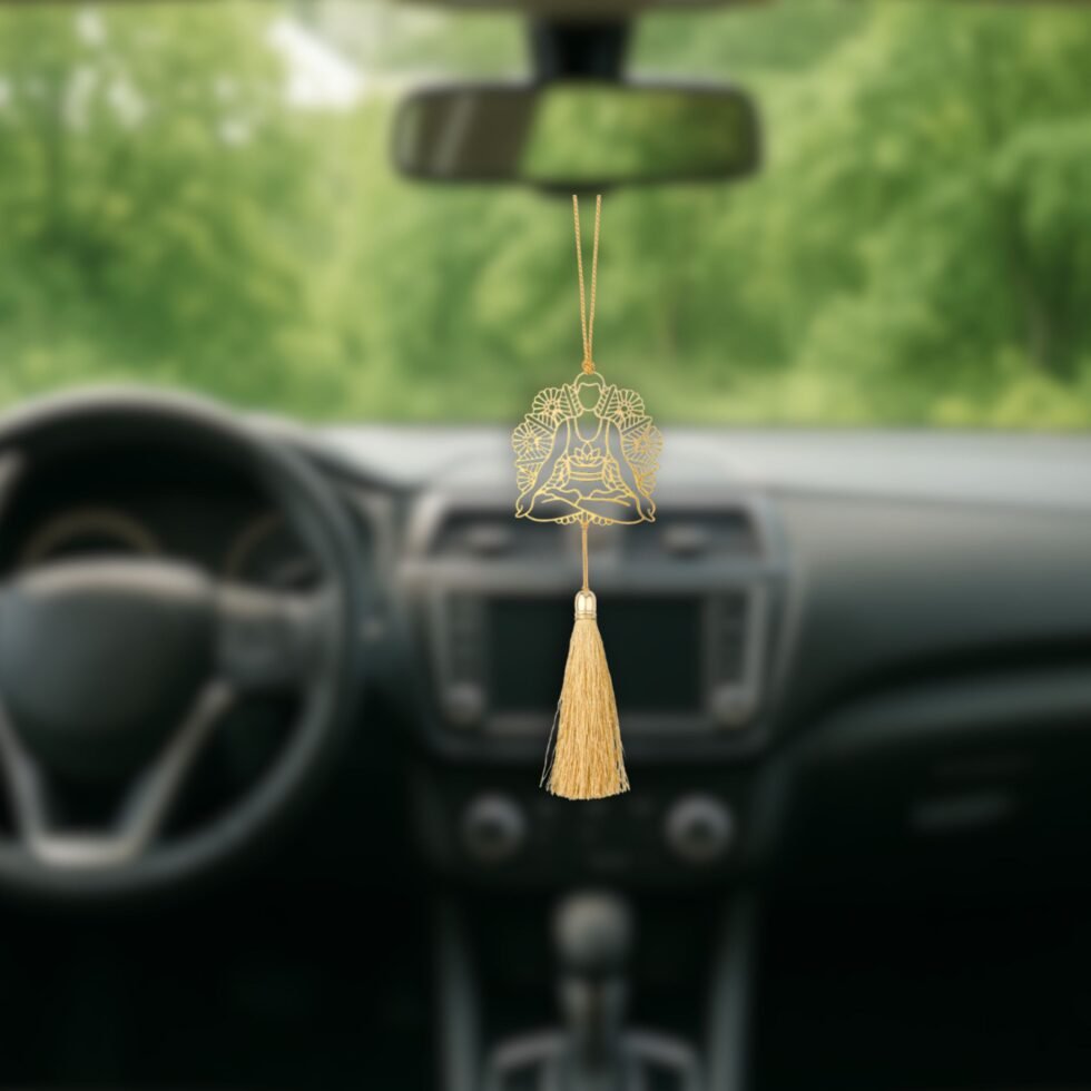 Gold plated yoga rear view mirror ornament hanging naturally inside a modern car with scenic road background.